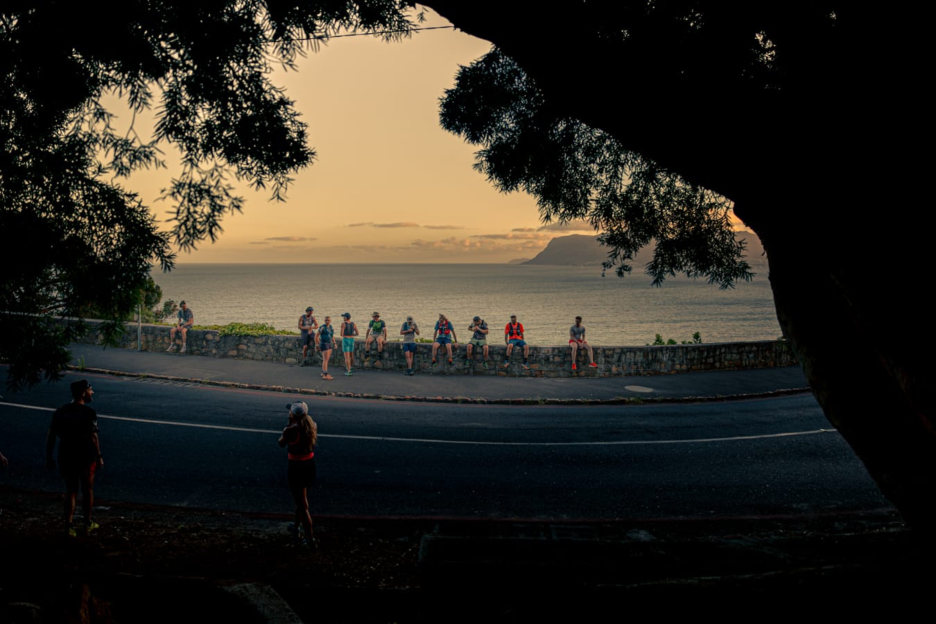 Trail runners silhouetted against ocean and mountains at golden hour
